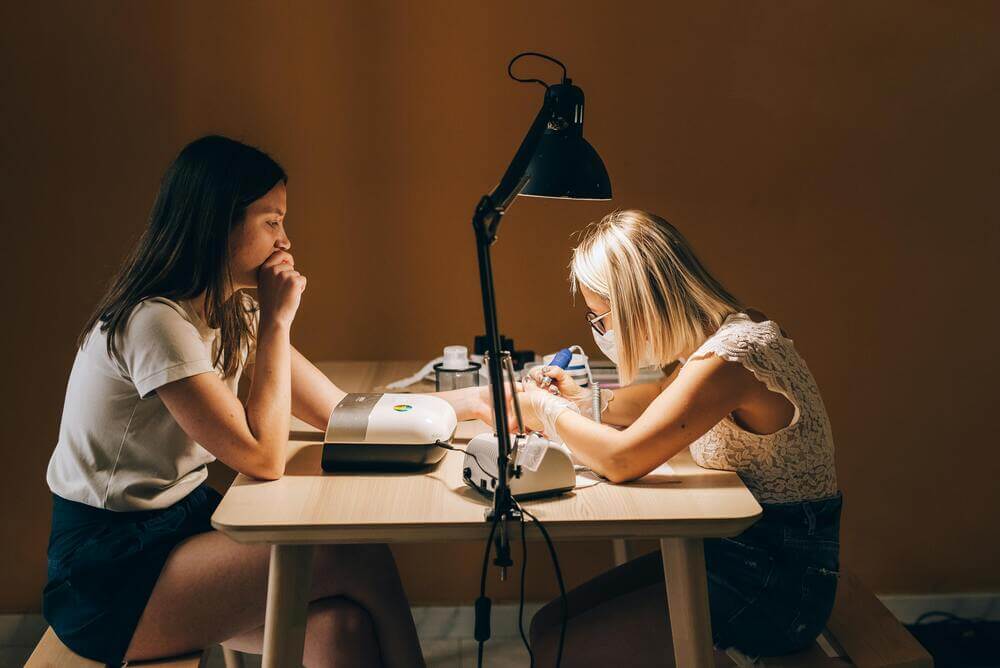 A nail artist doing a HEMA-free manicure on a woman in a salon.
